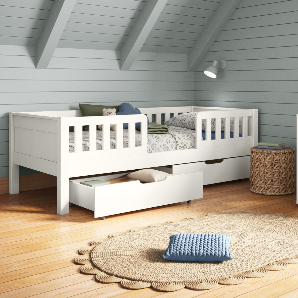 Closer view of Arven white Junior bed with safety guards and a pair of drawers styled with floral bedding in white, blue and green, in a child's bedroom with soft blue tongue and groove walls and slanted ceiling.